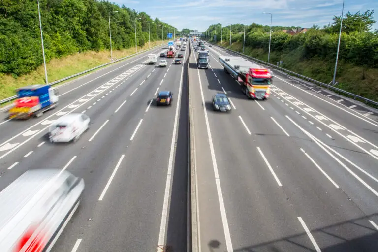An aerial photograph of a busy motorway in the UK with three lanes and a junction and traffic including cars and trucks speeding by with blurred motion